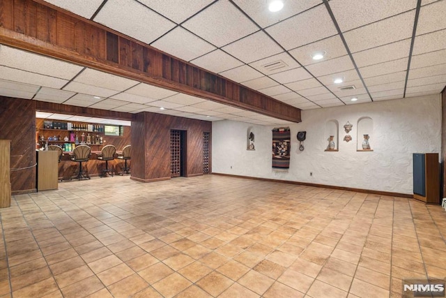 basement featuring a paneled ceiling, bar area, and wooden walls