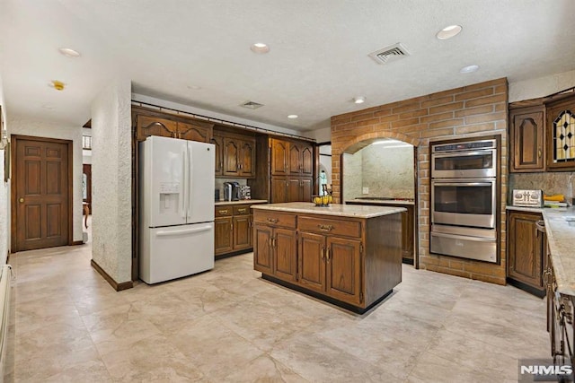 kitchen with white fridge with ice dispenser, double oven, and a center island