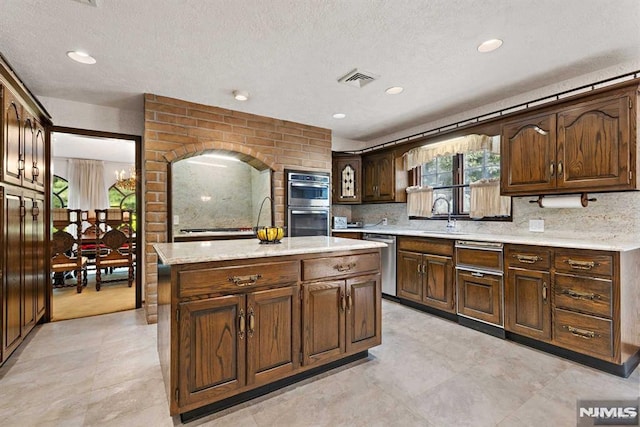 kitchen with sink, backsplash, light stone countertops, a kitchen island, and stainless steel appliances