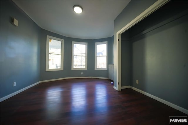 empty room with radiator heating unit and dark hardwood / wood-style flooring