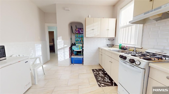 kitchen with light tile patterned floors, white gas range oven, white cabinets, washer / clothes dryer, and sink