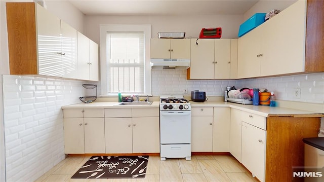 kitchen with a wealth of natural light, decorative backsplash, sink, and white range with gas cooktop