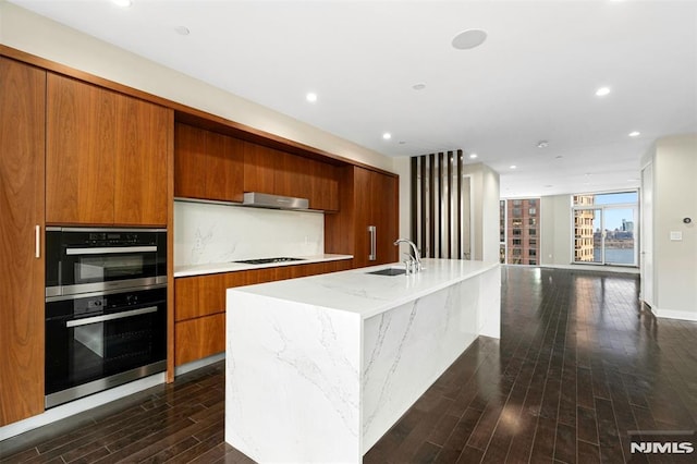 kitchen featuring sink, dark hardwood / wood-style flooring, double oven, black gas cooktop, and a kitchen island with sink