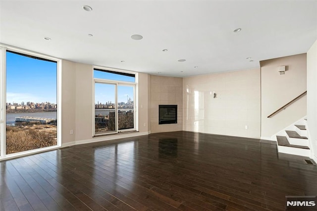 unfurnished living room featuring a water view, a fireplace, dark hardwood / wood-style flooring, and a wall of windows