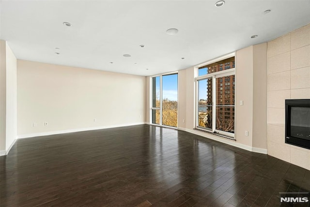 unfurnished living room with a tiled fireplace and dark wood-type flooring