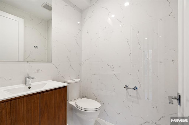 bathroom featuring vanity, toilet, and tile walls