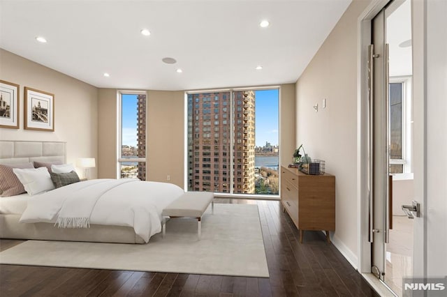 bedroom featuring a water view, dark wood-type flooring, and a wall of windows