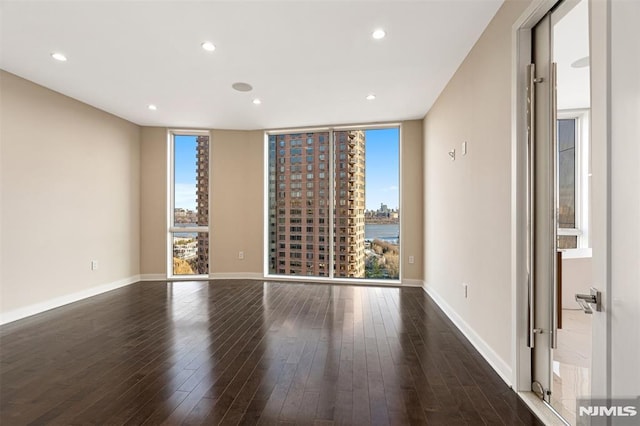 unfurnished room featuring dark hardwood / wood-style floors, floor to ceiling windows, and a water view