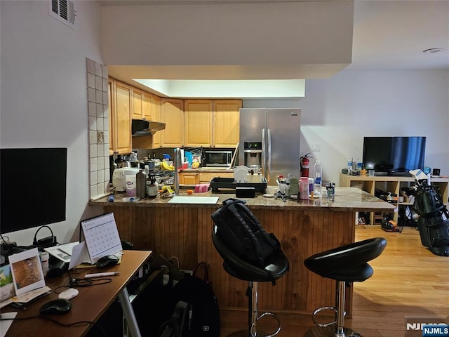 kitchen with stainless steel appliances, a breakfast bar, light hardwood / wood-style floors, and kitchen peninsula