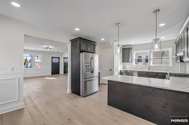 kitchen with pendant lighting, sink, light wood-type flooring, light stone counters, and stainless steel appliances