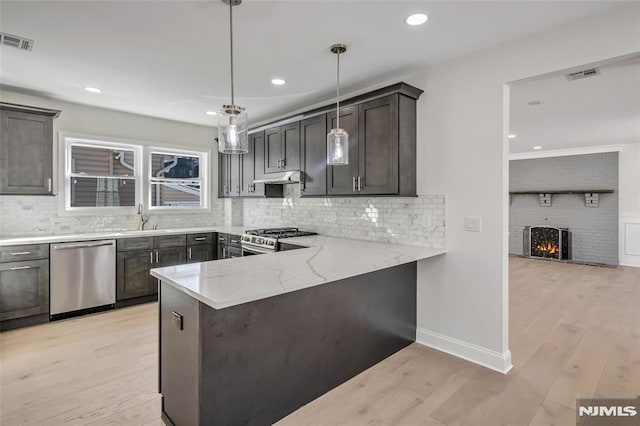 kitchen with kitchen peninsula, pendant lighting, light hardwood / wood-style flooring, sink, and stainless steel appliances