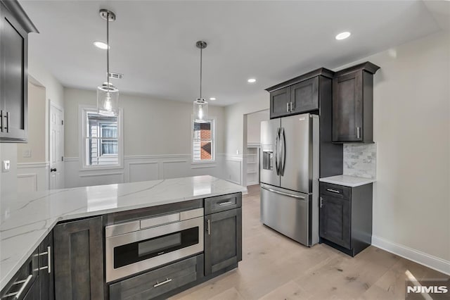 kitchen featuring decorative light fixtures, backsplash, appliances with stainless steel finishes, and light wood-type flooring