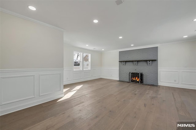 unfurnished living room featuring crown molding, light wood-type flooring, and a brick fireplace