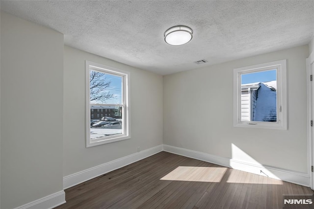 spare room with a textured ceiling and dark hardwood / wood-style flooring