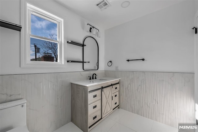 bathroom featuring vanity, toilet, tile walls, and tile patterned flooring