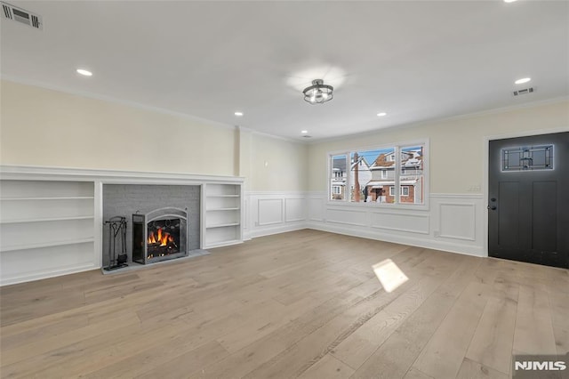 unfurnished living room featuring built in shelves, a brick fireplace, light hardwood / wood-style flooring, and crown molding