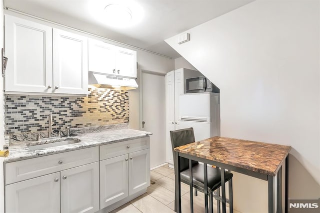 kitchen featuring tasteful backsplash, sink, white cabinetry, light tile patterned floors, and light stone counters