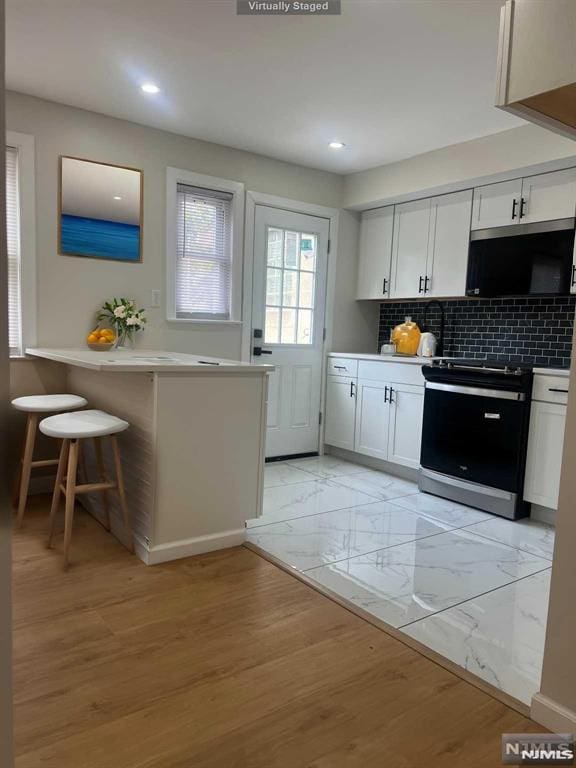 kitchen with electric stove, tasteful backsplash, kitchen peninsula, a kitchen breakfast bar, and white cabinets