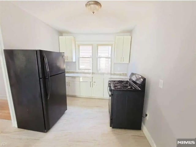 kitchen with black refrigerator, white cabinets, and gas range