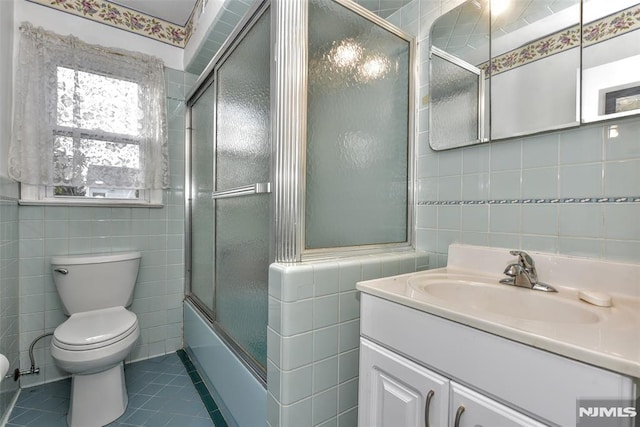 full bathroom with shower / bath combination with glass door, tile patterned flooring, vanity, tile walls, and toilet