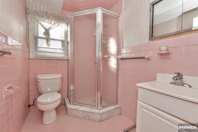 bathroom with a shower with door, tile patterned flooring, tile walls, toilet, and vanity