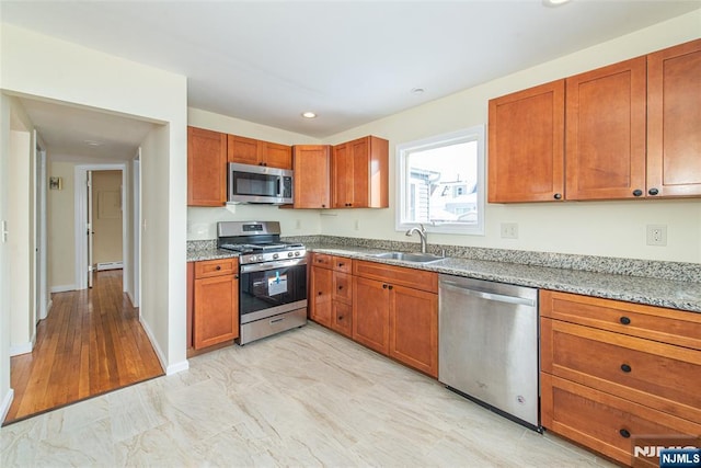 kitchen with sink, light stone counters, light hardwood / wood-style flooring, and appliances with stainless steel finishes