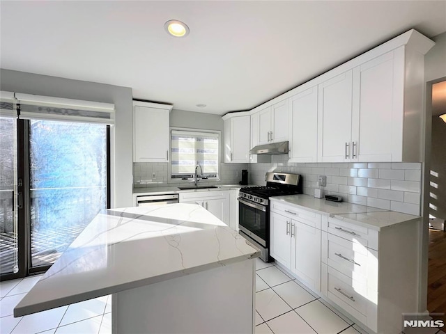 kitchen with tasteful backsplash, a center island, sink, stainless steel gas stove, and light stone counters