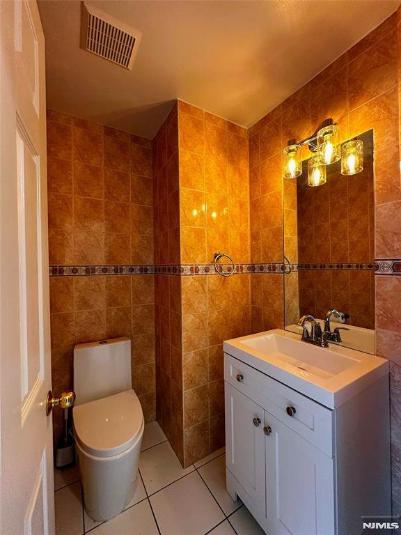 bathroom with toilet, vanity, tile walls, and tile patterned floors