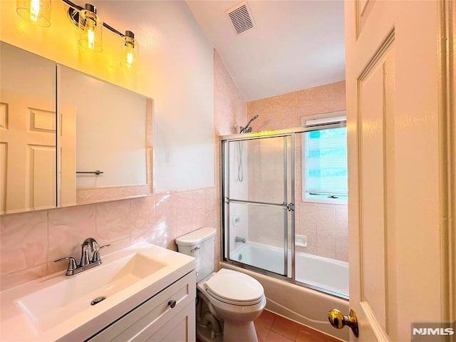 full bathroom with shower / bath combination with glass door, tile patterned flooring, vanity, tile walls, and toilet