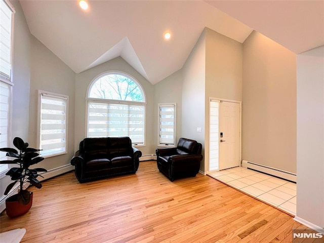 living room featuring high vaulted ceiling, a baseboard heating unit, and light hardwood / wood-style flooring