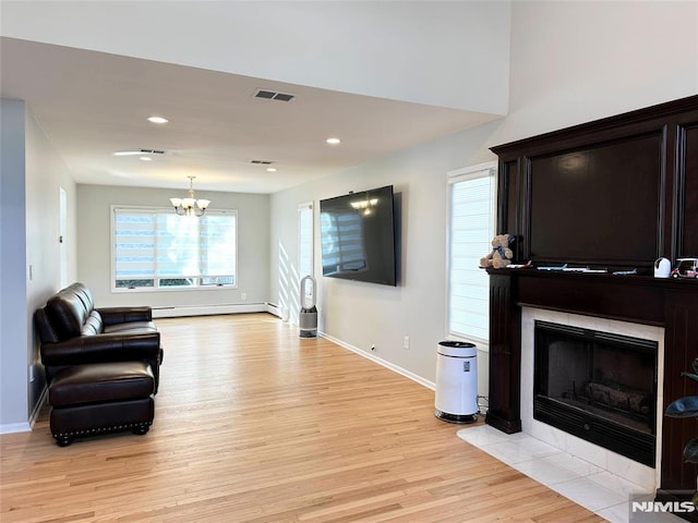 living room featuring light hardwood / wood-style floors, a baseboard heating unit, a notable chandelier, and a fireplace