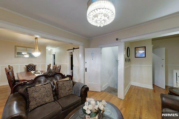 living room featuring light wood-type flooring, a chandelier, a barn door, and crown molding