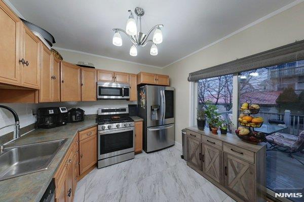 kitchen with hanging light fixtures, appliances with stainless steel finishes, sink, a notable chandelier, and ornamental molding