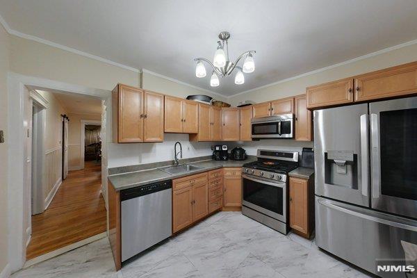 kitchen featuring appliances with stainless steel finishes, a chandelier, sink, decorative light fixtures, and ornamental molding