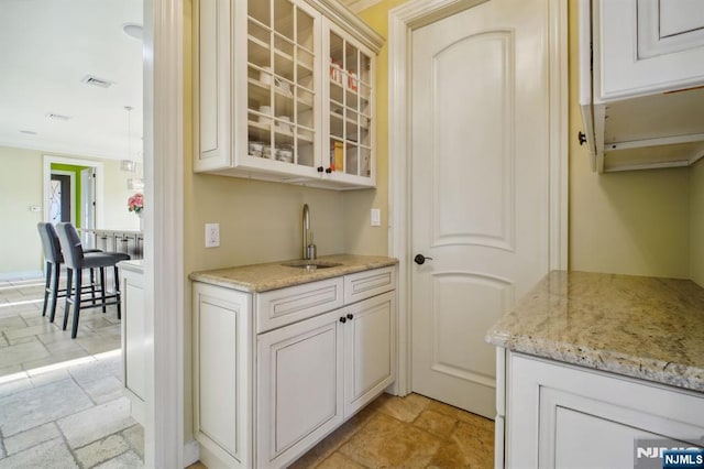 bar with light stone counters, sink, and white cabinets