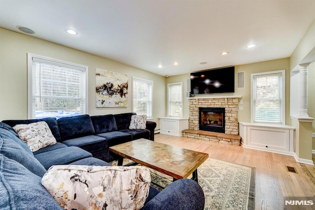 living room with ornate columns, light hardwood / wood-style floors, and a stone fireplace