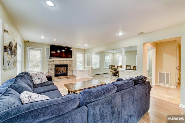 living room with a baseboard radiator, light hardwood / wood-style flooring, and a stone fireplace