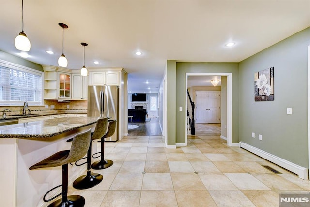 kitchen with dark stone countertops, decorative backsplash, hanging light fixtures, stainless steel refrigerator, and a breakfast bar area