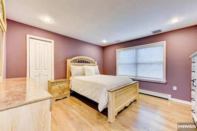 bedroom with a baseboard heating unit, a closet, and light hardwood / wood-style floors