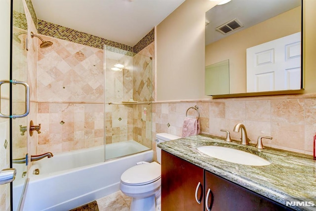 full bathroom with shower / bath combination with glass door, tile patterned flooring, vanity, tile walls, and toilet