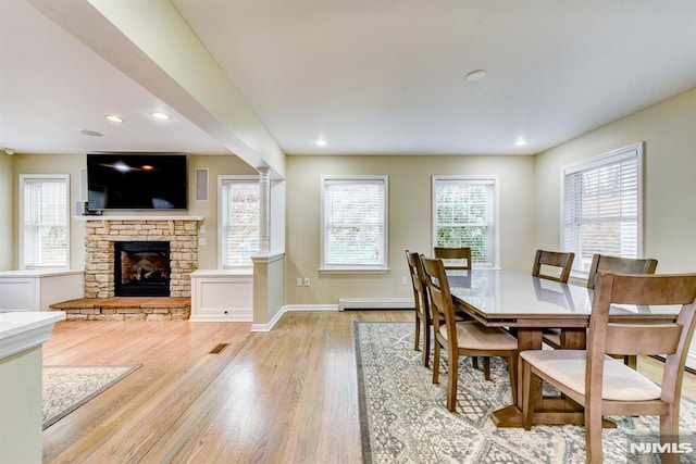 dining space with a fireplace, a baseboard heating unit, a healthy amount of sunlight, and light wood-type flooring