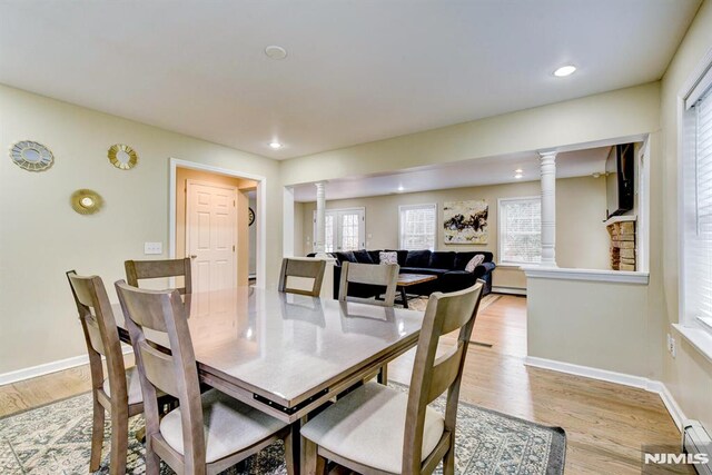 dining area featuring light wood-type flooring, ornate columns, and a baseboard radiator