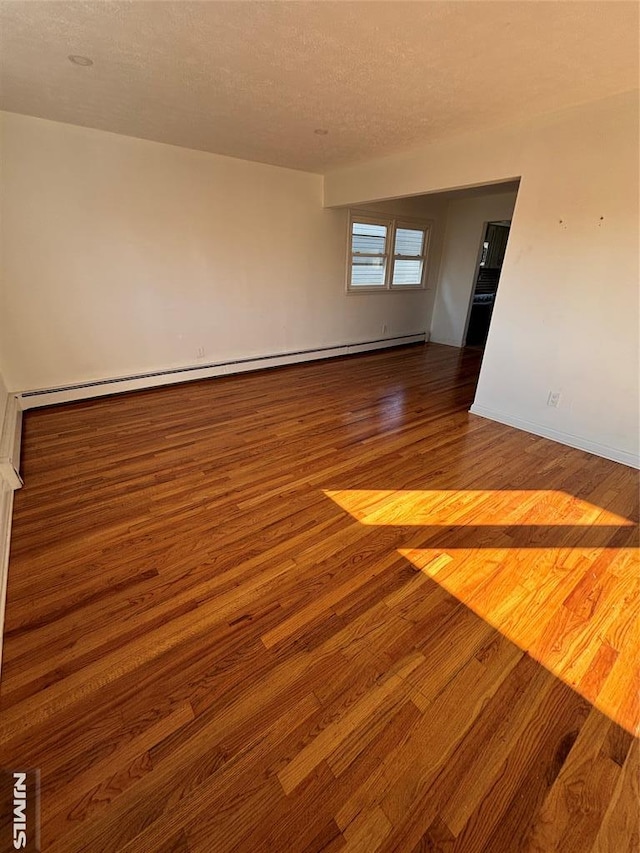 empty room with baseboard heating, wood-type flooring, and a textured ceiling