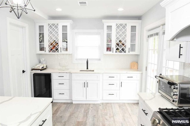 kitchen featuring light stone counters, sink, white cabinetry, and light wood-type flooring