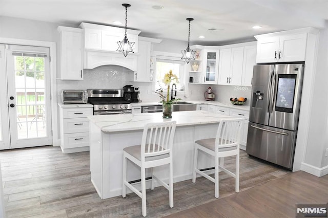 kitchen with white cabinets, appliances with stainless steel finishes, hardwood / wood-style flooring, and a center island