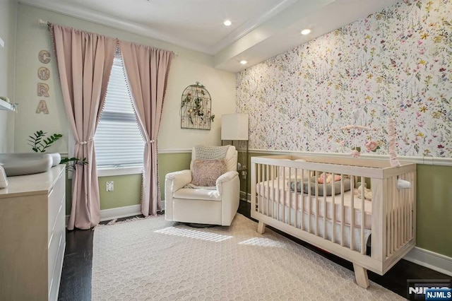 bedroom featuring a nursery area, crown molding, and hardwood / wood-style floors