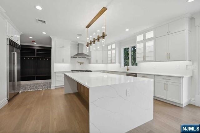 kitchen with wall chimney exhaust hood, white cabinetry, high quality fridge, a large island, and light hardwood / wood-style floors