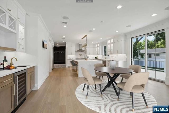 dining room featuring crown molding, beverage cooler, light hardwood / wood-style floors, and wet bar