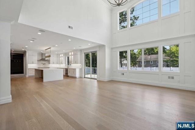 unfurnished living room with an inviting chandelier, light wood-type flooring, and a high ceiling