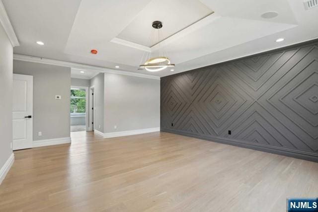 spare room featuring ornamental molding, a raised ceiling, and light wood-type flooring